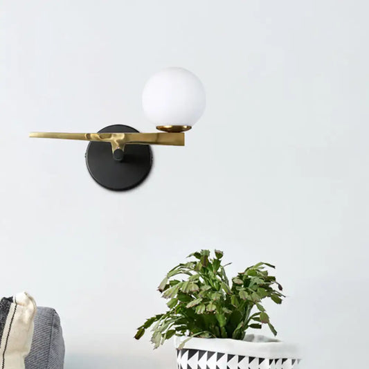 Modern black and brass wall sconce with a matte base and white glass ball shade for bedroom lighting