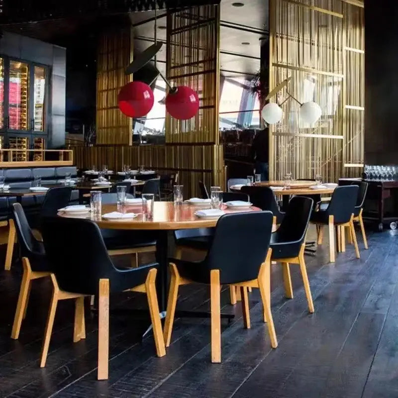 Black upholstered chairs with light wood legs arranged around tables under a decorbites glass cherry pendant light in a modern dining room