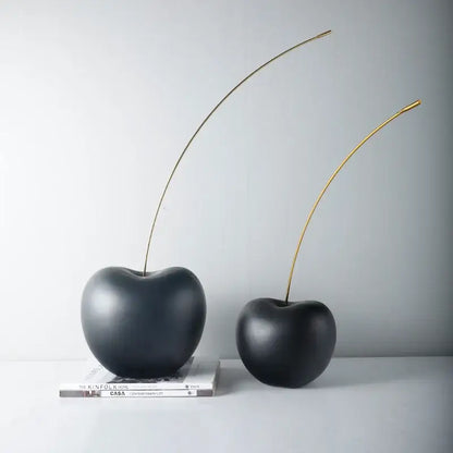 Two glossy black cherry resin sculptures with slender gold stems displayed on stacked books for modern decorbites decor