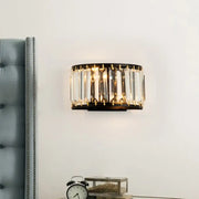 A modern black and gold wall lamp with vertical crystal prisms designed as a bedroom light fixture