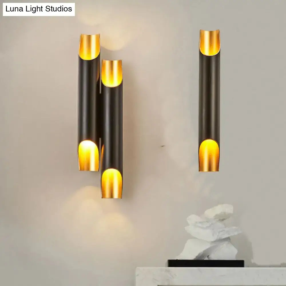 Modern black and gold tubular aluminum wall sconce with sleek cylindrical design emitting warm glow for living room