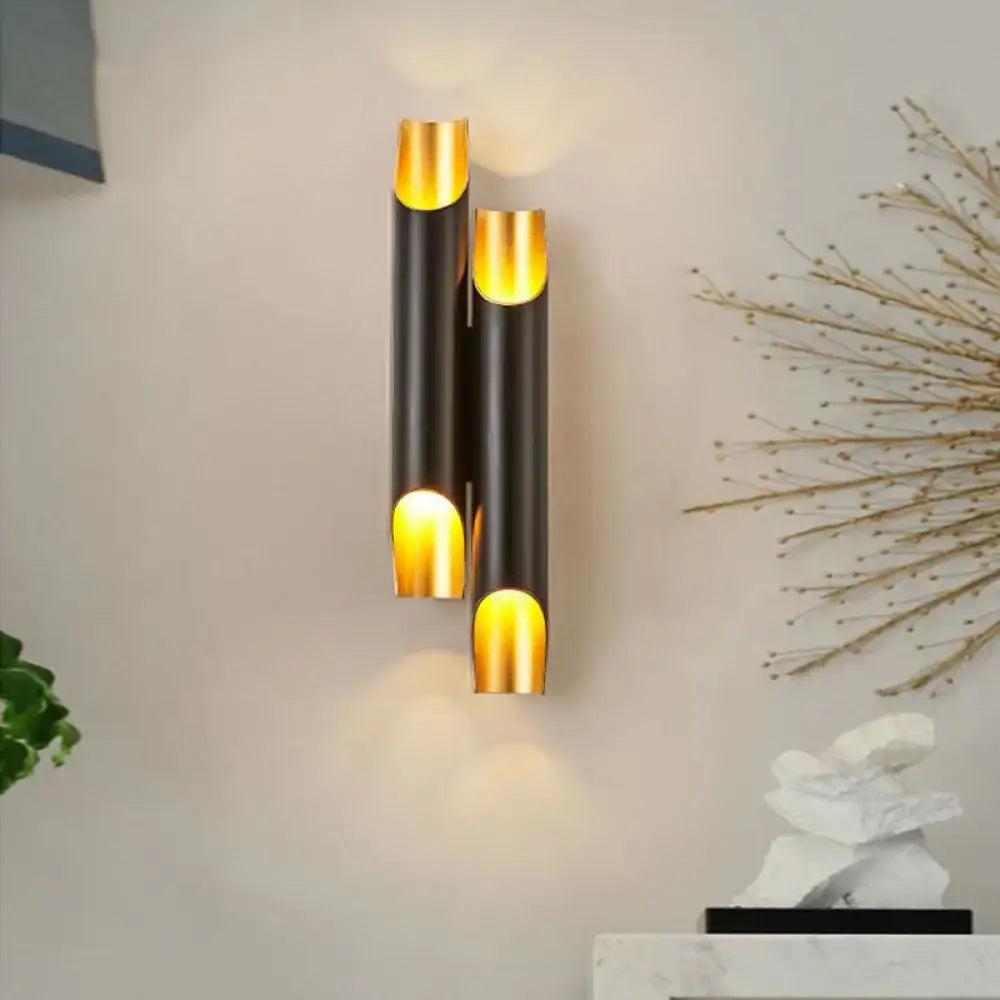Modern black and gold tubular aluminum wall sconce with three vertical tubes emitting warm glow for living room use