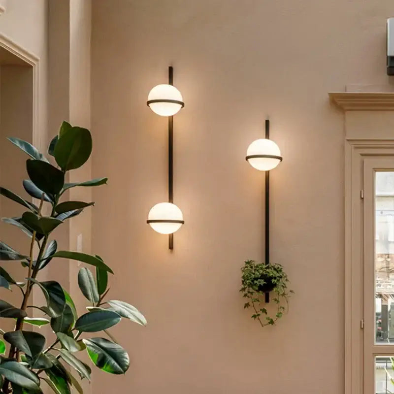 Three modern black wall lights with sleek stems and glowing white acrylic ball shades for bedroom sconces