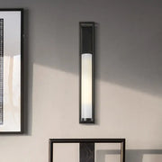 Modern black and white glass tubular wall mount bedroom sconce with frosted glass diffuser emitting warm light