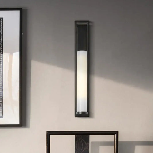 Modern black and white glass tubular wall mount bedroom sconce with frosted glass diffuser emitting warm light