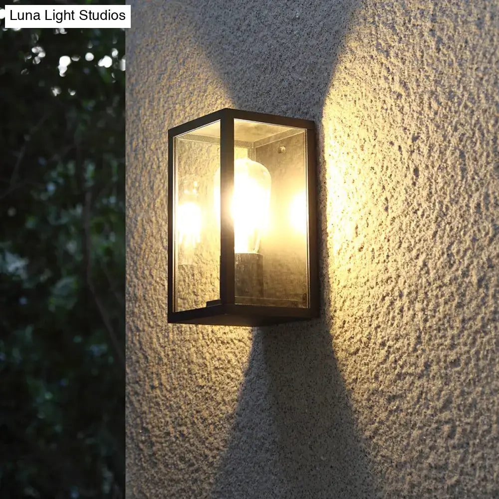Modern black box patio wall sconce with clear glass panels and warm glowing bulb for outdoor lighting fixture