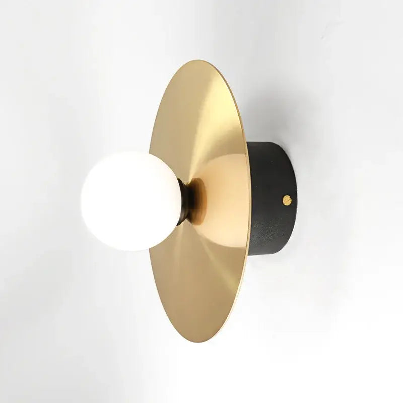 Modern black and brass wall light fixture with a brushed gold circular shade and white glass ball bulb for bedroom decorbites