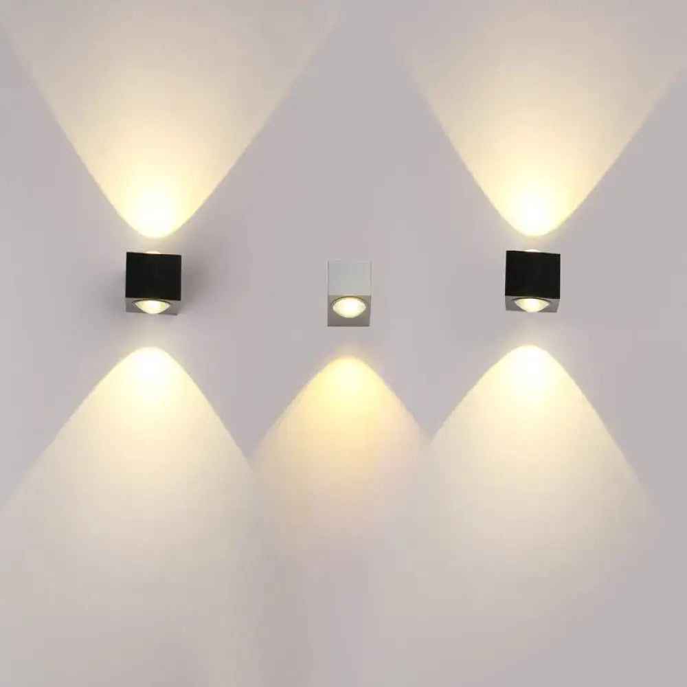Three modern square rgb wall lighting pieces in black matte and brushed silver finish emit warm yellow light in a corridor
