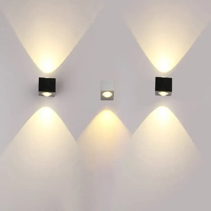 Three modern square rgb wall lighting pieces in black matte and brushed silver finish emit warm yellow light in a corridor