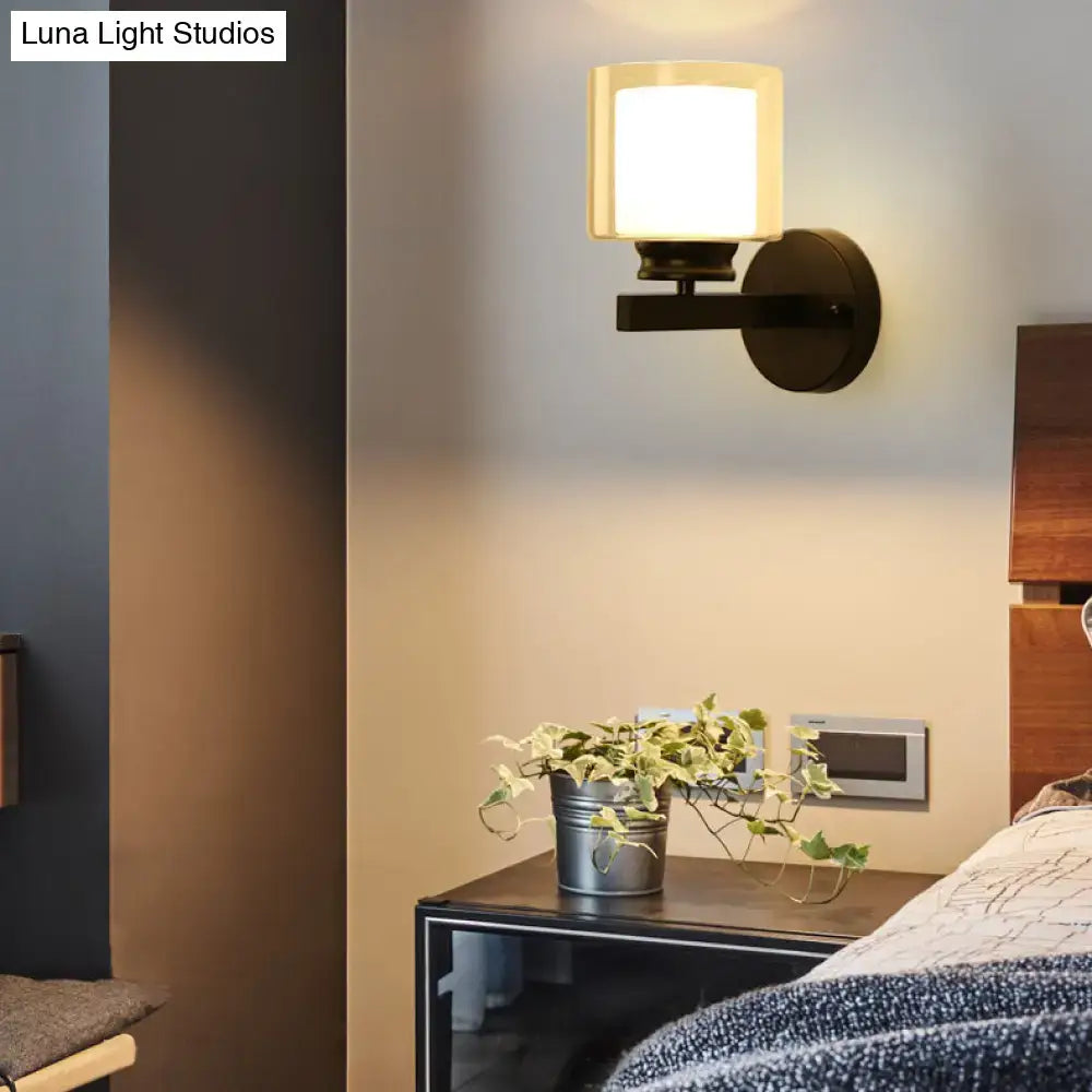 Modern black wall mounted clear glass sconce with warm-toned cylindrical frosted shade and matte metal arm