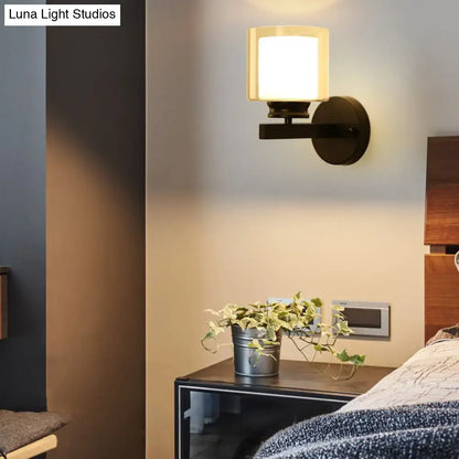 Modern black wall mounted clear glass sconce with warm-toned cylindrical frosted shade and matte metal arm