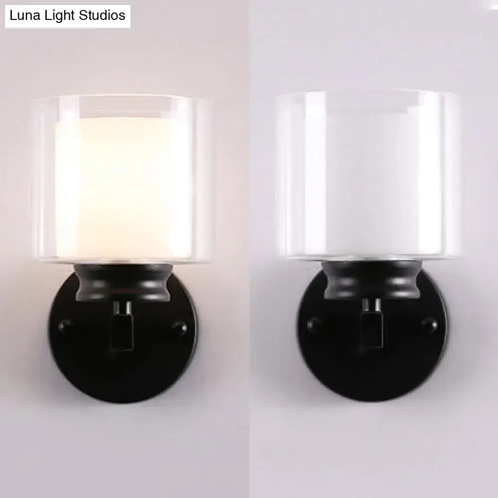 Modern black and chrome wall mounted clear glass sconce with a cylindrical glass shade and frosted white interior for bedroom lighting