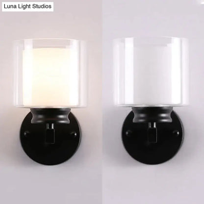 Modern black and chrome wall mounted clear glass sconce with a cylindrical glass shade and frosted white interior for bedroom lighting