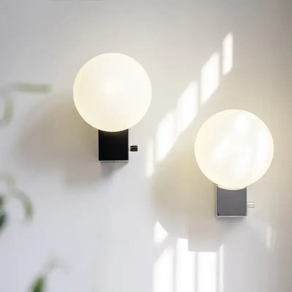 Two minimalist decorbites glass ball wall sconces with black and chrome bases for modern bedroom lighting