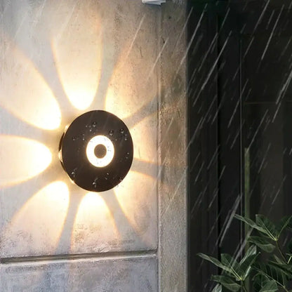 Modern black circular led outdoor wall sconce with an illuminated ring casting warm radial beams on outdoor wall