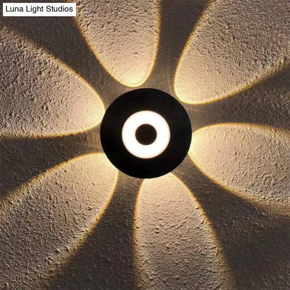 Modern black circular led outdoor wall sconce with glowing white ring emitting warm petal-shaped light patterns for outdoor wall use