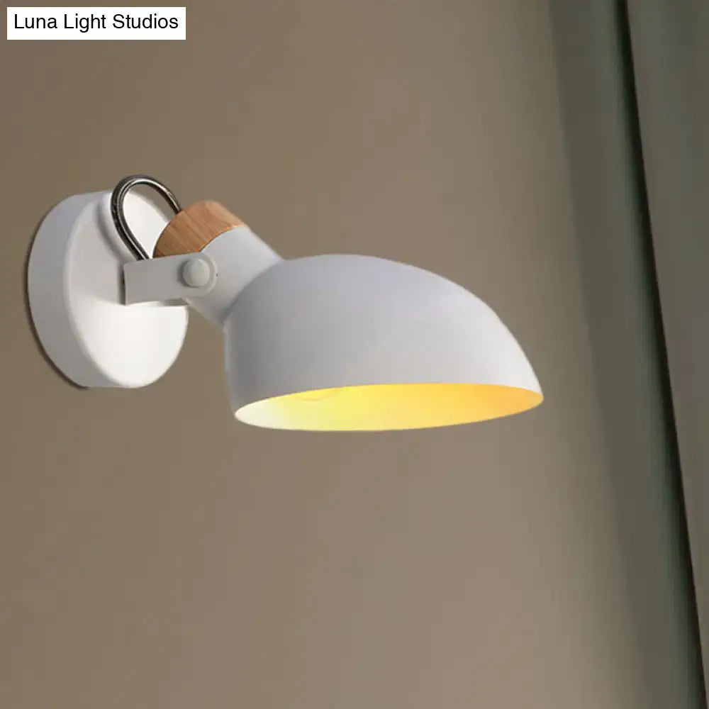 Modern black and cream wall sconce light with wooden accent and adjustable arm emitting warm yellow light in bedroom