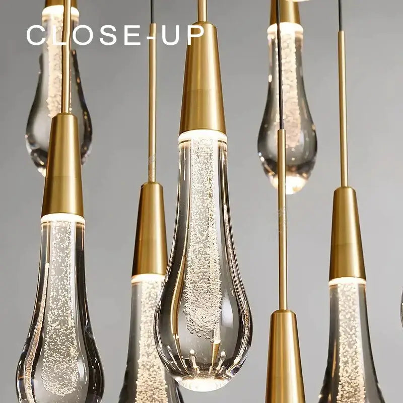 Modern black crystal chandelier light fixture with gold-toned pendant lights and clear glass teardrop shades filled with sparkling liquid