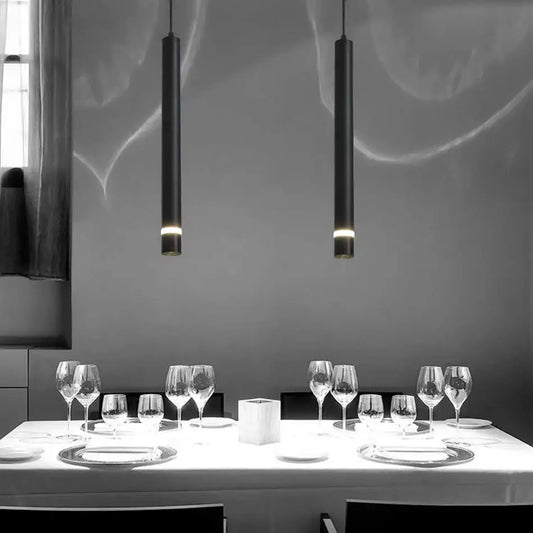 Two sleek black decorbites cylinder pipe pendant lights hang above a dining table for modern dining room decor