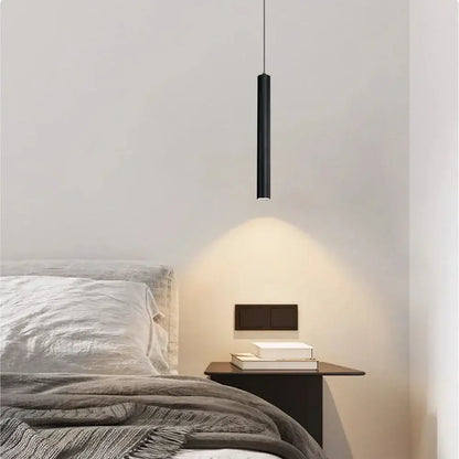 Modern black cylindrical cord pendant light with sleek minimalist design hanging above bedside table in bedroom