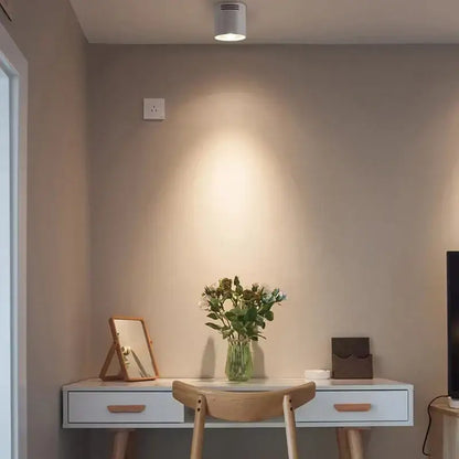 A modern black cylindrical pendant ceiling spot light illuminating a clear glass vase with greenery and white flowers