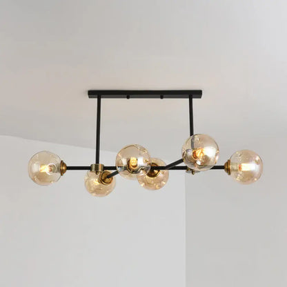 Modern black island pendant light with six amber glass globes and brass accents for dining room or kitchen island lighting