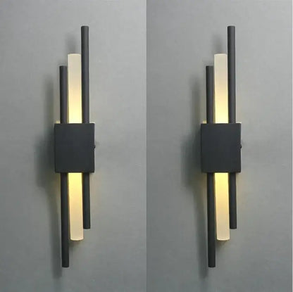Modern black and gold acrylic pipe wall lamp with three vertical rods and frosted glass panels emitting warm glow