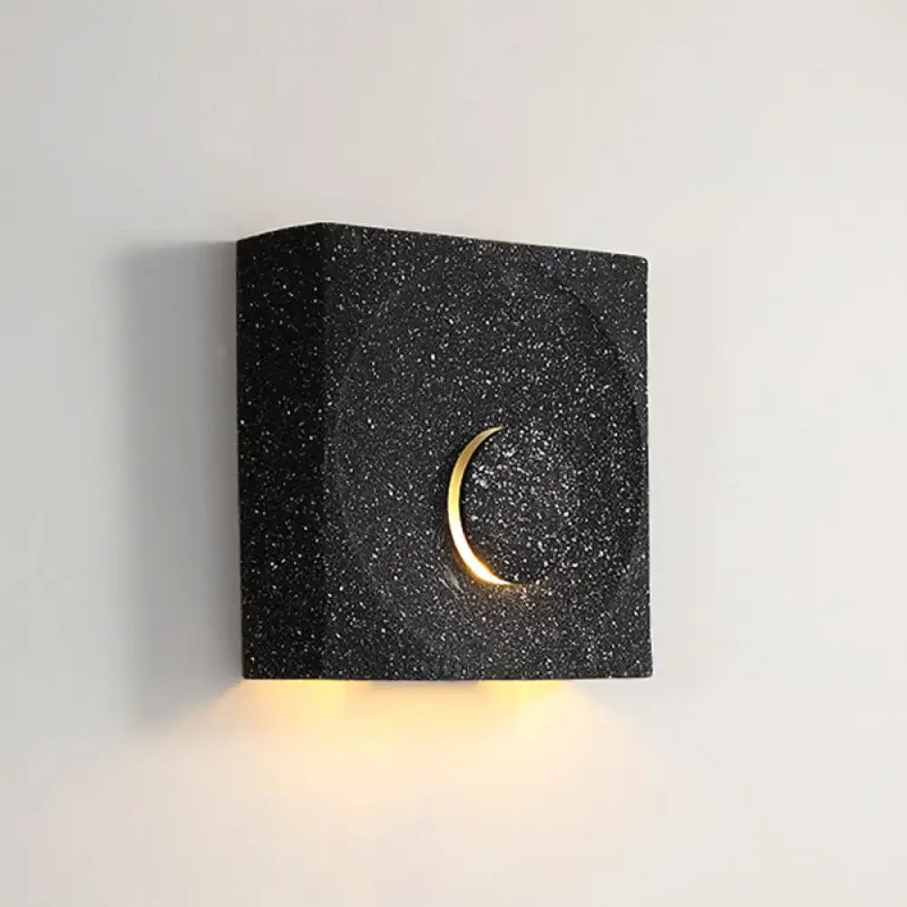 Modern black and gold cement square wall light with crescent moon design emitting warm light for bedroom use