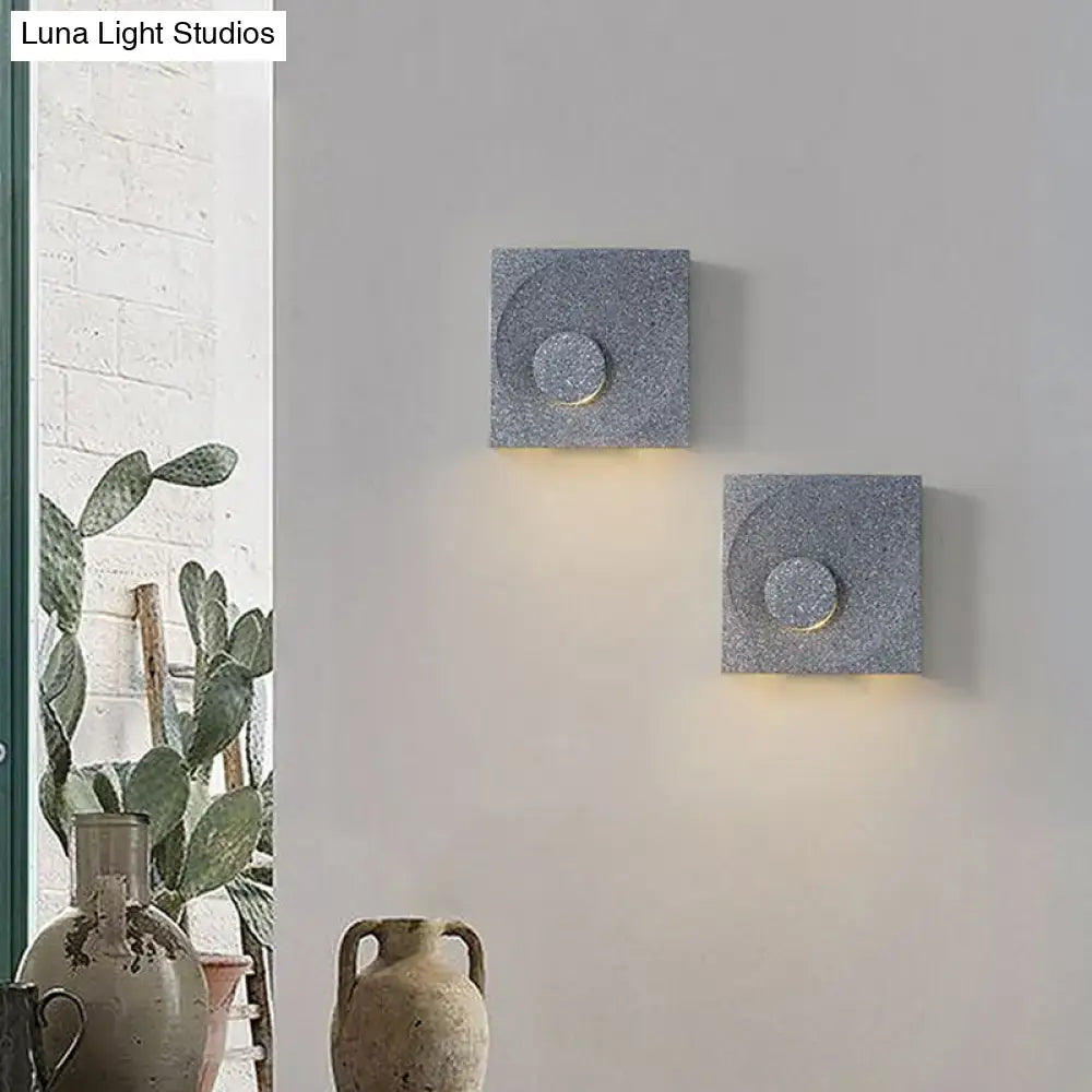 Modern black and gold cement square wall light with gray stone circular cutouts and warm light for bedroom use