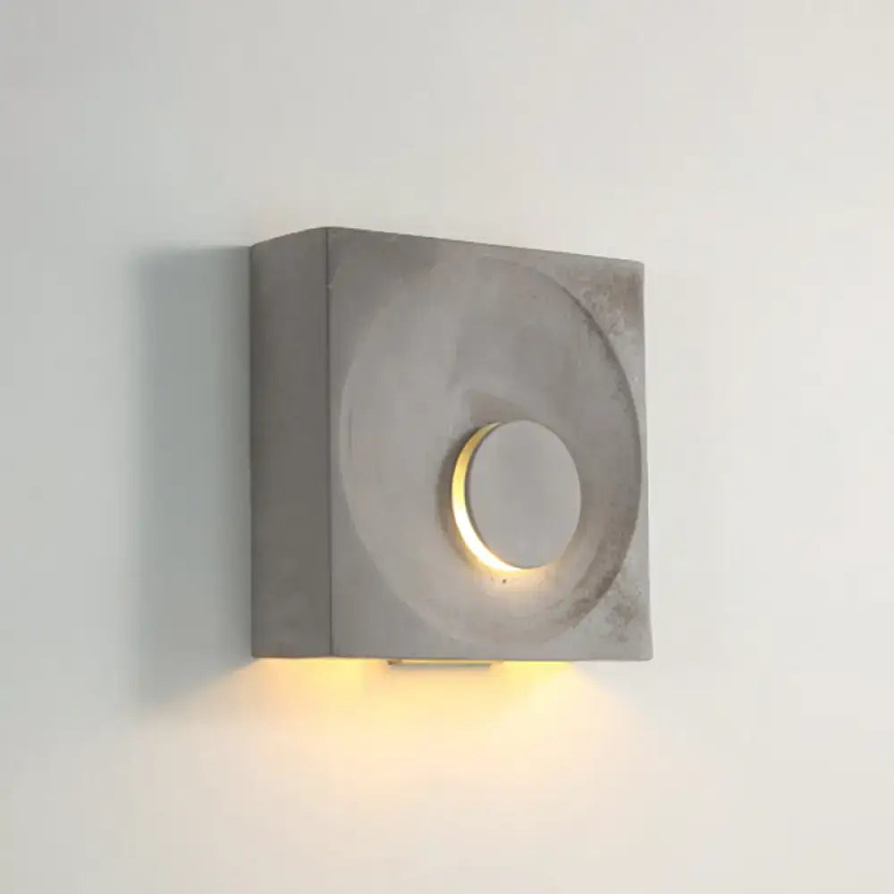 Modern black and gold cement square wall light with gray concrete sconce and circular cutout emitting warm light type