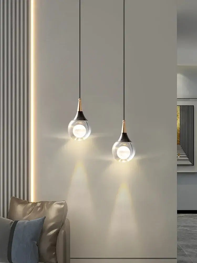 Two modern black and gold crystal led ball pendant lights with clear glass globes and brass accents hang from black cords