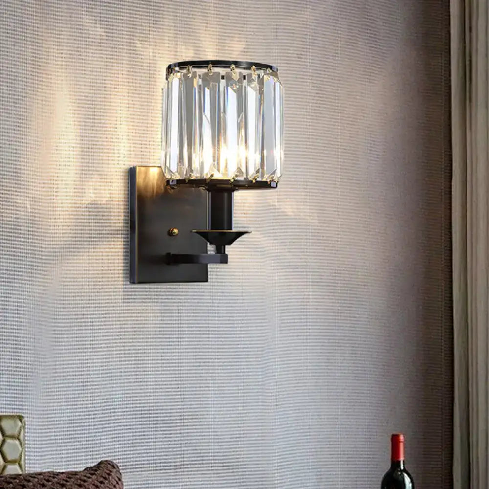 Modern black and gold sconce light fixture with cylindrical crystal shade for wired electric power bedroom use