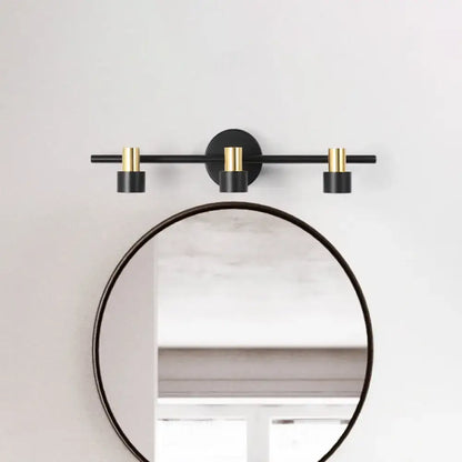 Modern black and gold cylinder wall light with three sleek cylindrical bulbs for bedroom vanity use