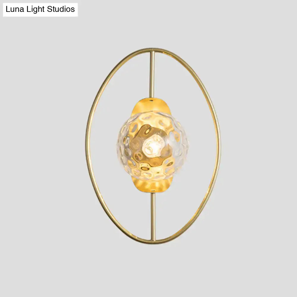 Modern black and gold wall lamp featuring a gold-toned oval frame and a textured translucent white glass globe fixture type