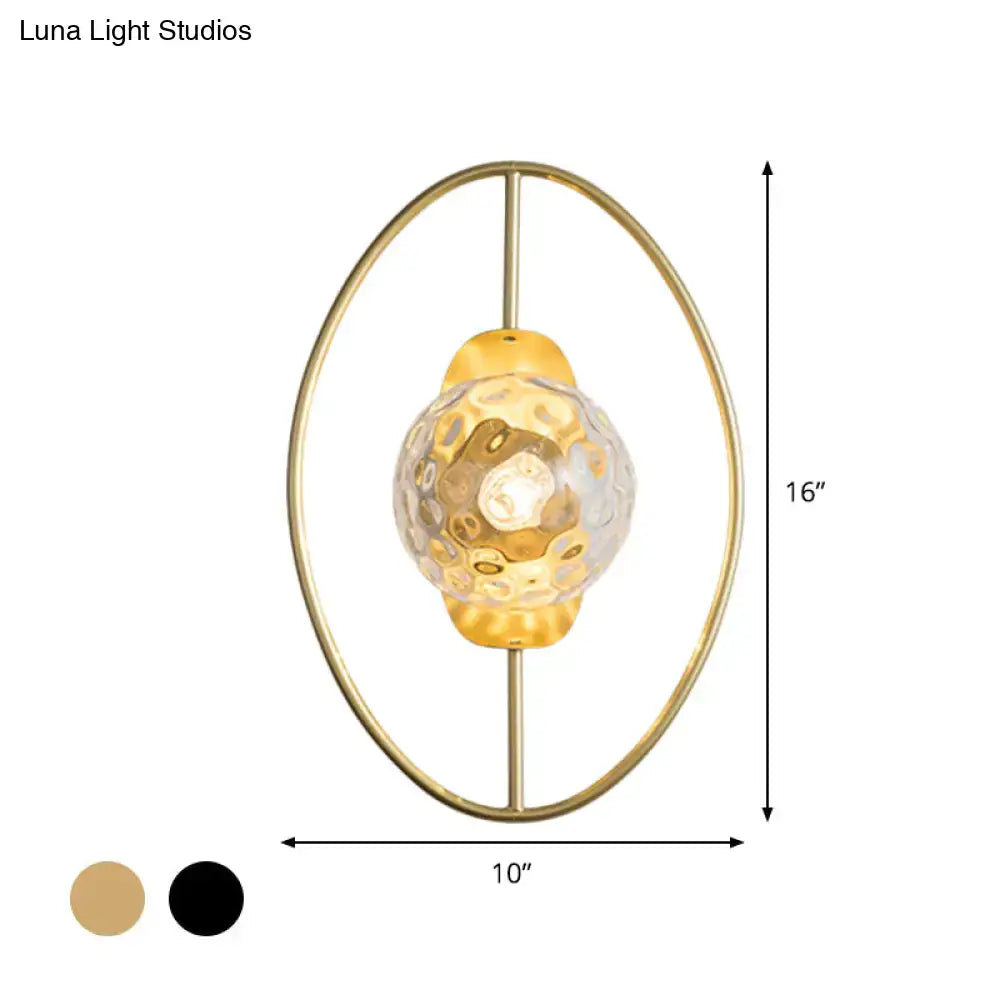 Modern black and gold wall lamp with gold-toned oval metal frame and textured translucent white glass globe fixture