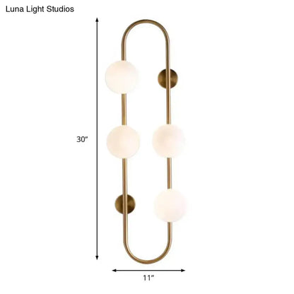 Brass-finished wall sconce with four frosted white glass globe shades in a modern curved globe wall sconce design