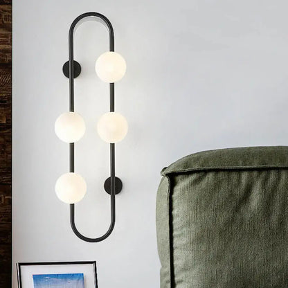 Modern black metal wall sconce with four white glass globe lights in a curved globe wall sconce design for bedroom
