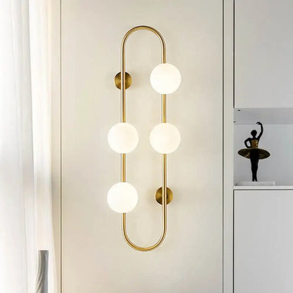 Modern black and gold globe wall sconce with four white glass frosted bulbs in a curved design for bedroom lighting