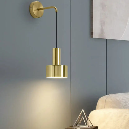 Gold-finished minimalist wall lamp with sleek curved arm and cylindrical shade for modern bedroom reading light