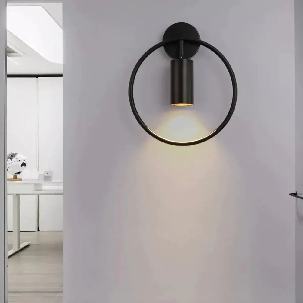 Modern black and gold irwin wall lamp with a matte circular ring and cylindrical light fixture for bedroom use