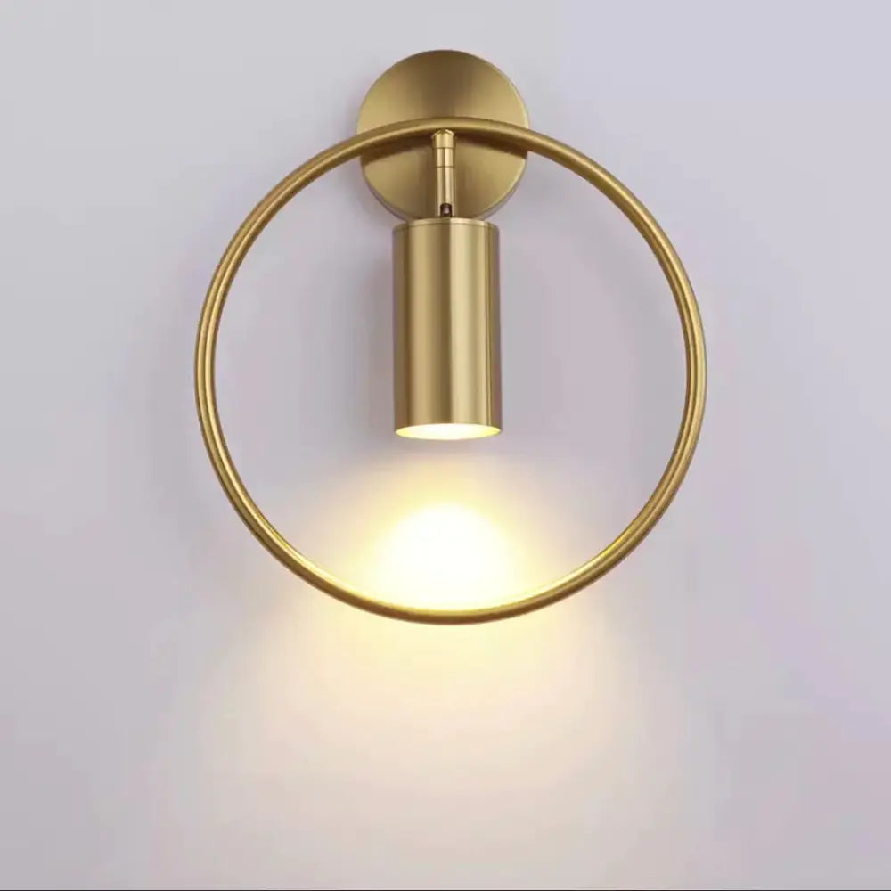 Gold-toned circular irwin wall lamp with cylindrical light fixture and minimalist design for modern bedroom sconce