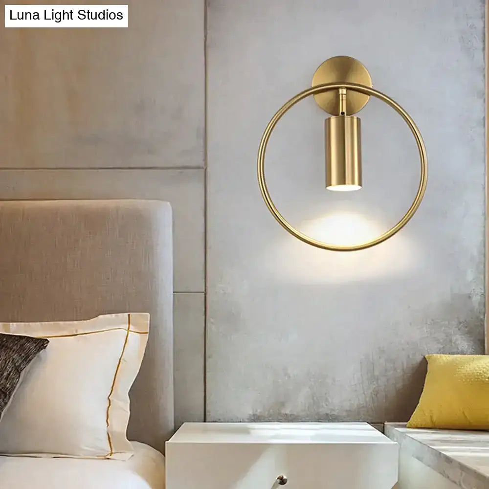 Gold-toned circular wall lamp with cylindrical light fixture and minimalist design in modern irwin wall lamp style