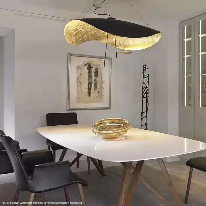 A modern black and gold leaf pendant light with metallic gold texture hangs above a dining table for living room decorbites decor