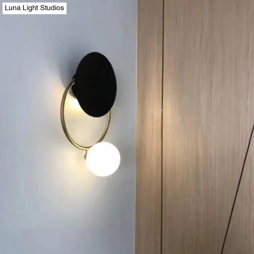 Modern black and gold metal planet wall mount lamp with circular shade and glowing white spherical bulb for bedroom sconce