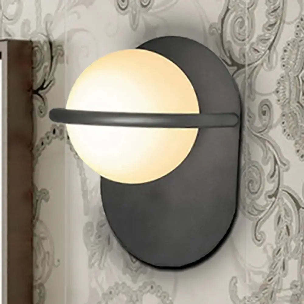 Modern black wall light with warm glowing milk glass shade and metal backplate suitable for bedroom lighting