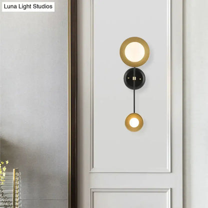 Gold-toned circular wall sconce with black mounting plate and milky glass for modern bedroom reading lamp