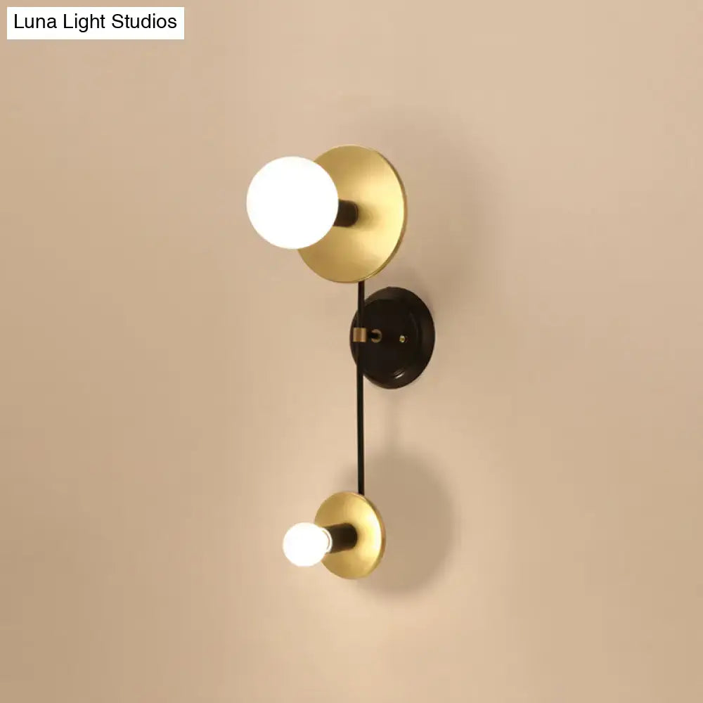 Modern black and gold wall sconce with milky glass globe bulbs and a black central mounting plate for bedroom reading