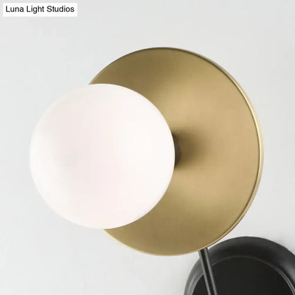 A modern black and gold wall sconce with a brass finish and frosted milky glass shade for bedroom reading