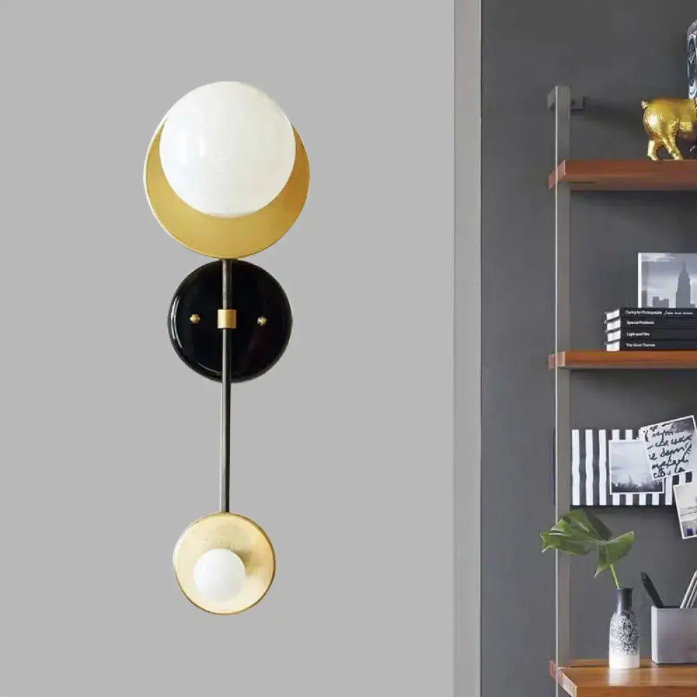 Modern black and gold wall sconce with milky glass spherical shades on a curved arm for bedroom reading lighting