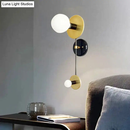 Modern black and gold wall sconce with milky glass spherical shades and matte black circular base for bedroom reading